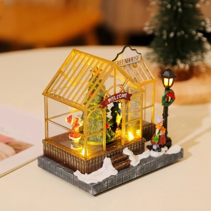 estufa de natal com música acesa sobre a mesa ao lado de mini pinheiro